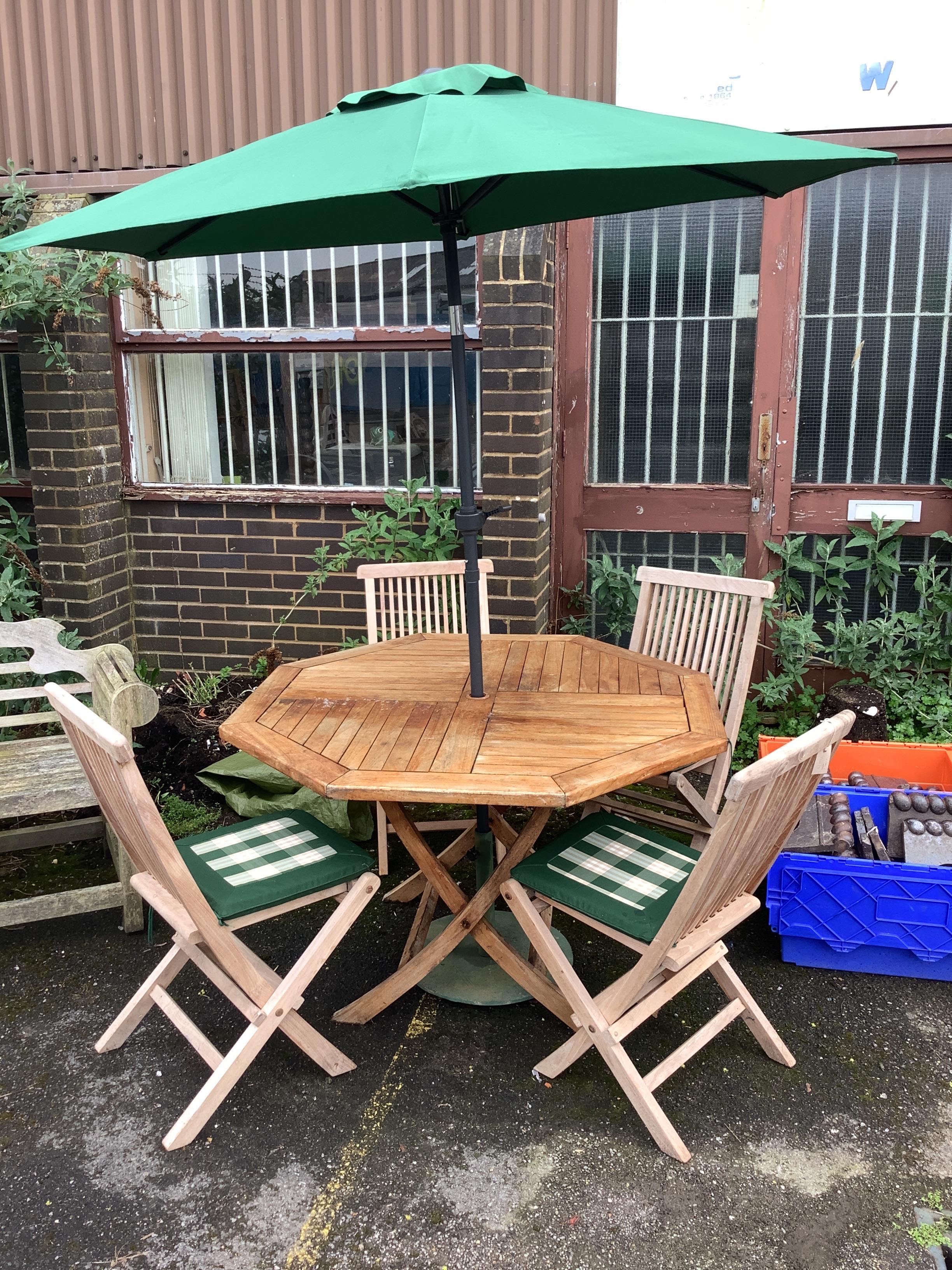 An octagonal weathered teak folding garden table, width 120cm, height 76cm four teak folding chairs with seat cushions and a parasol with cast metal base